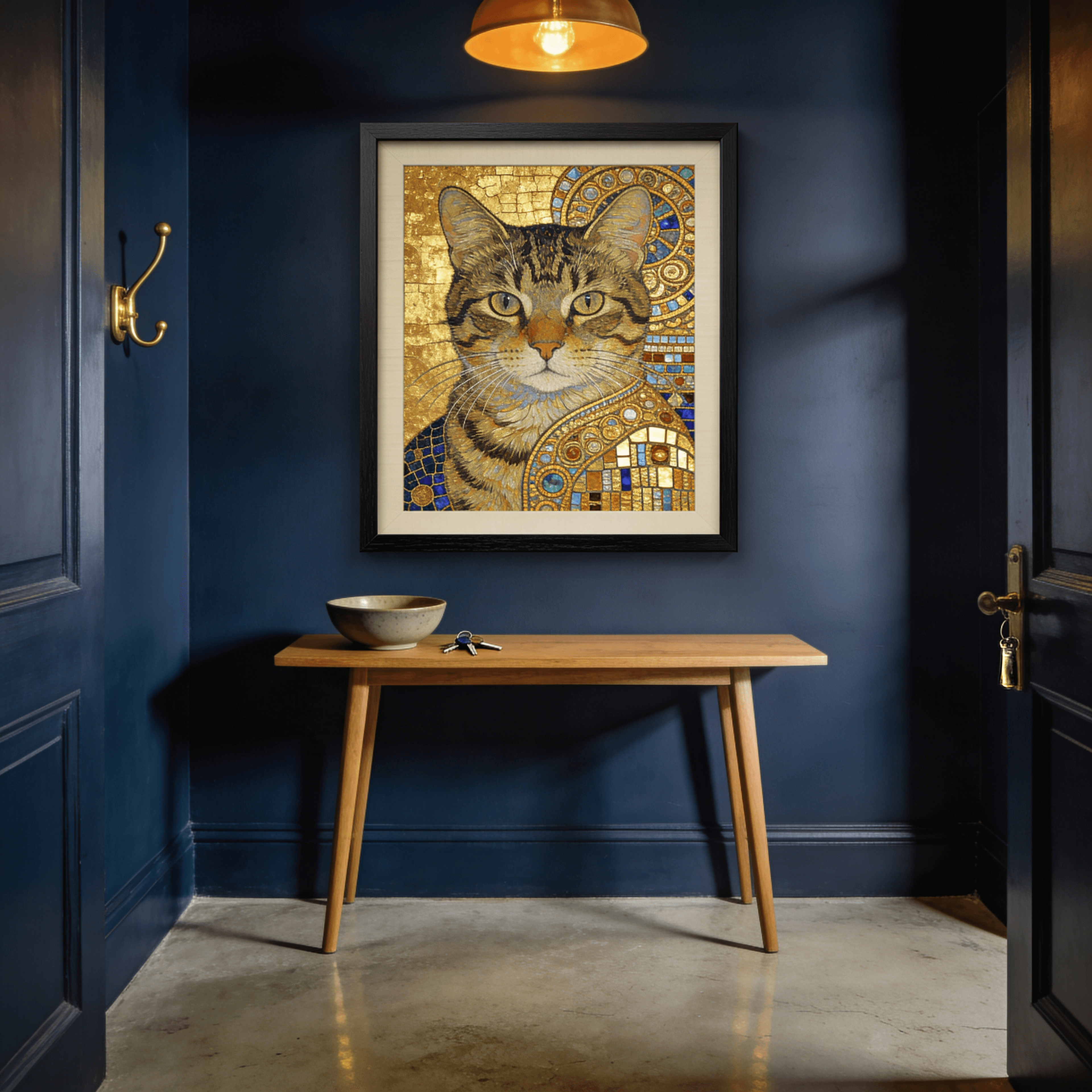 A Klimt gold-leaf portrait of a tabby cat in a black hardwood frame, hanging in a deep navy entryway above an oak console table